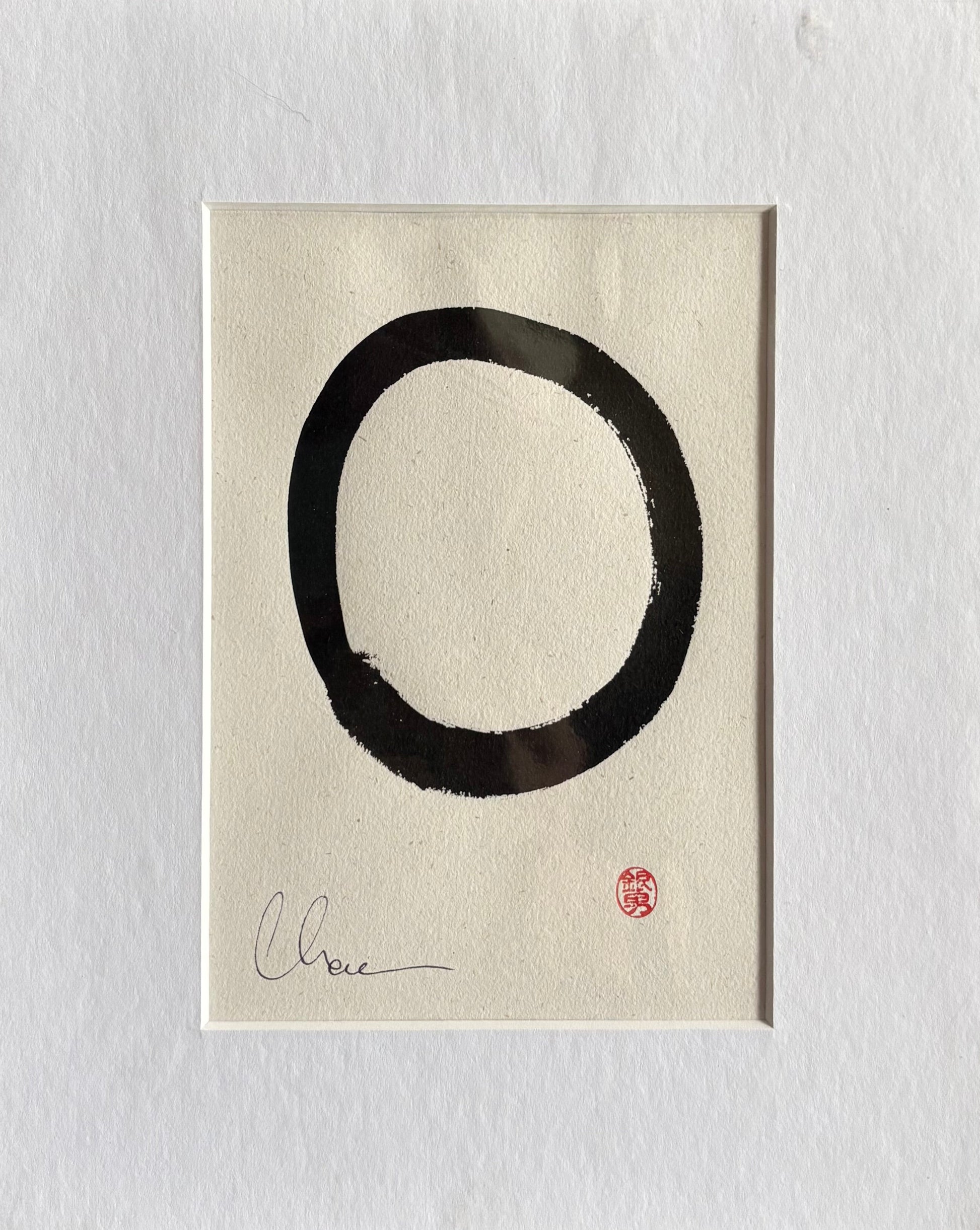Black circular brushstroke on beige paper with a signature and seal, framed in white.
